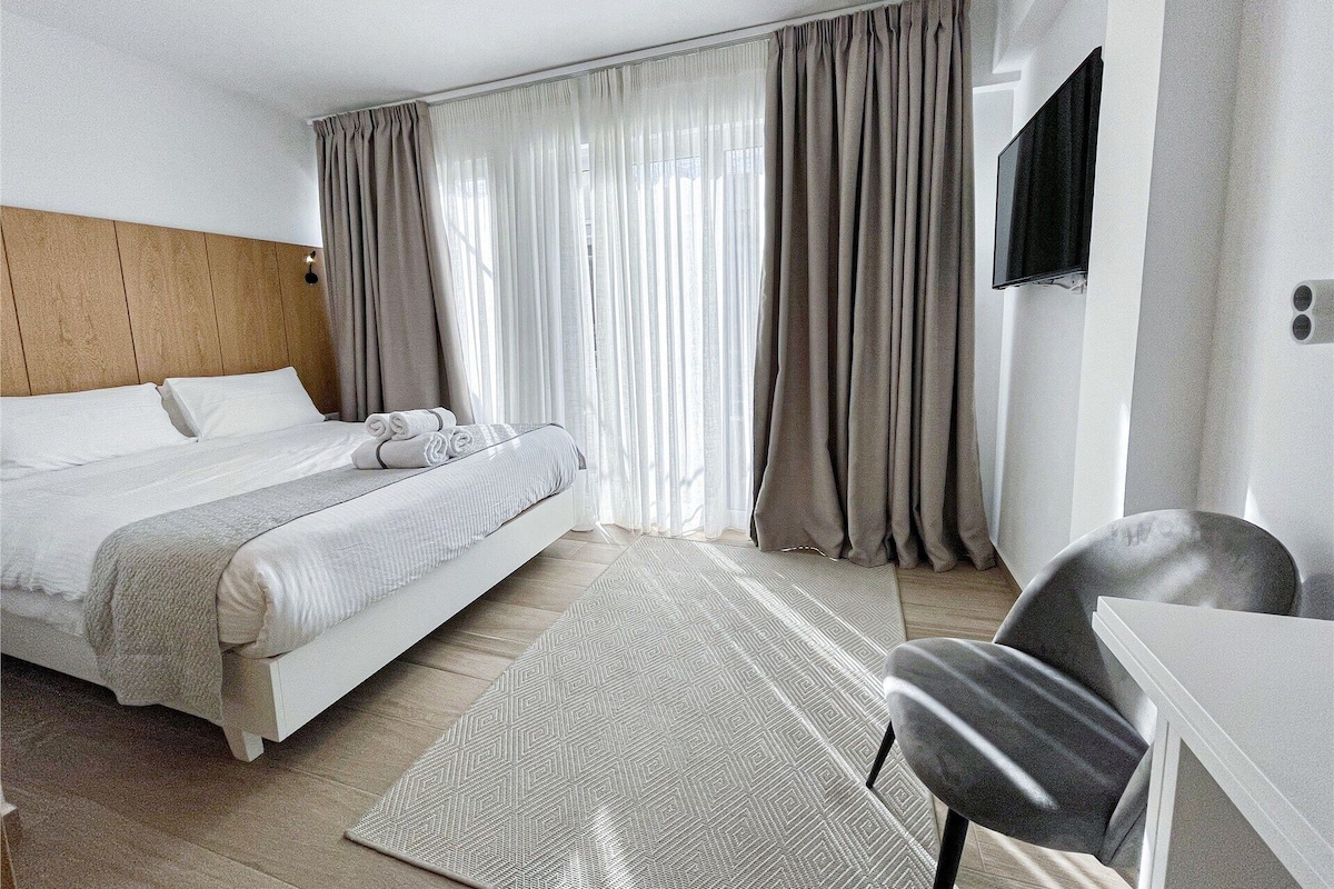 Hotelkamer met een bed, bureau, stoel, televisie en gordijnen.