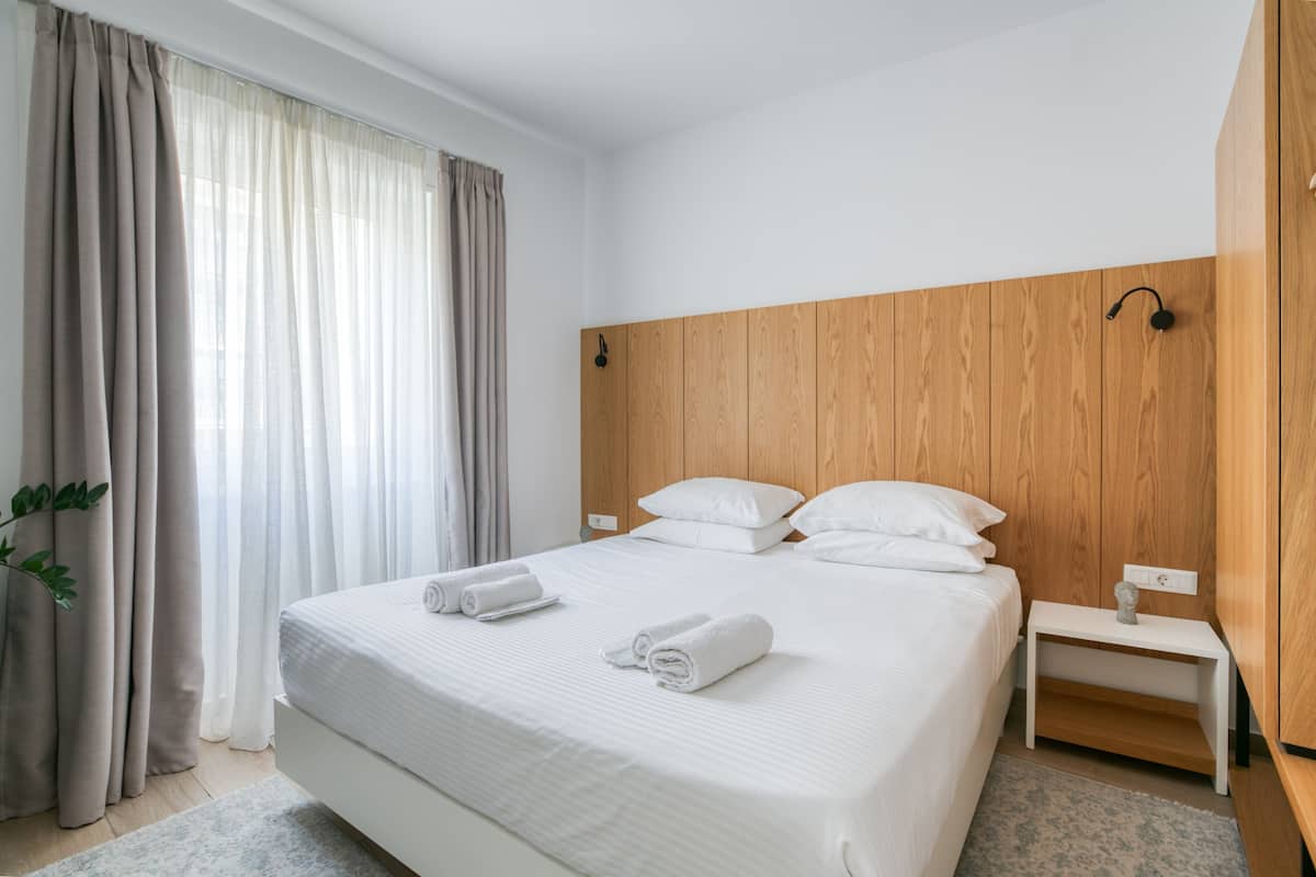 Une chambre d’hôtel moderne avec un grand lit, une tête de lit en bois et une table de chevet avec une lampe.