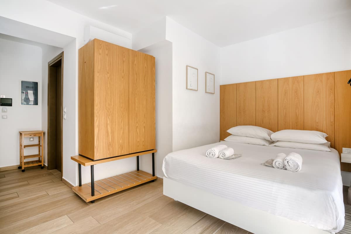 Une chambre d’hôtel moderne avec une armoire en bois, un lit où les serviettes sont soigneusement pliées, et une petite table d’appoint en bois.