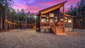 A log cabin with a stone foundation, wooden exterior, and a porch with a staircase. - Ride to ATV Trails + Dog Run + Game Room + Bunk Bed Nook + Guests Favorite (Broken Bow)