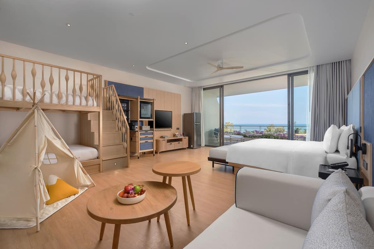 A modern hotel room with a bed, a seating area, a TV, and a balcony with a view.