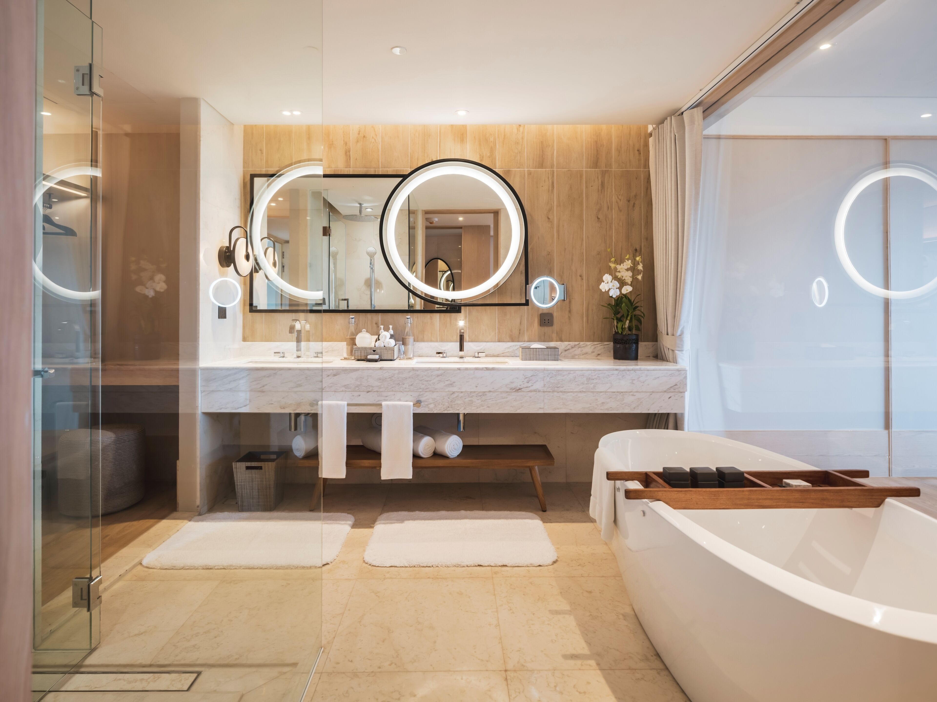 A modern bathroom with a large mirror, two sinks, a bathtub, and a potted orchid.