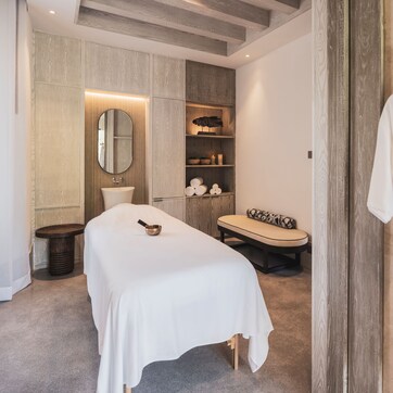 A modern bedroom with a large bed, a bedside table, a mirror, a vanity with a sink, and a robe hanging on a hook.