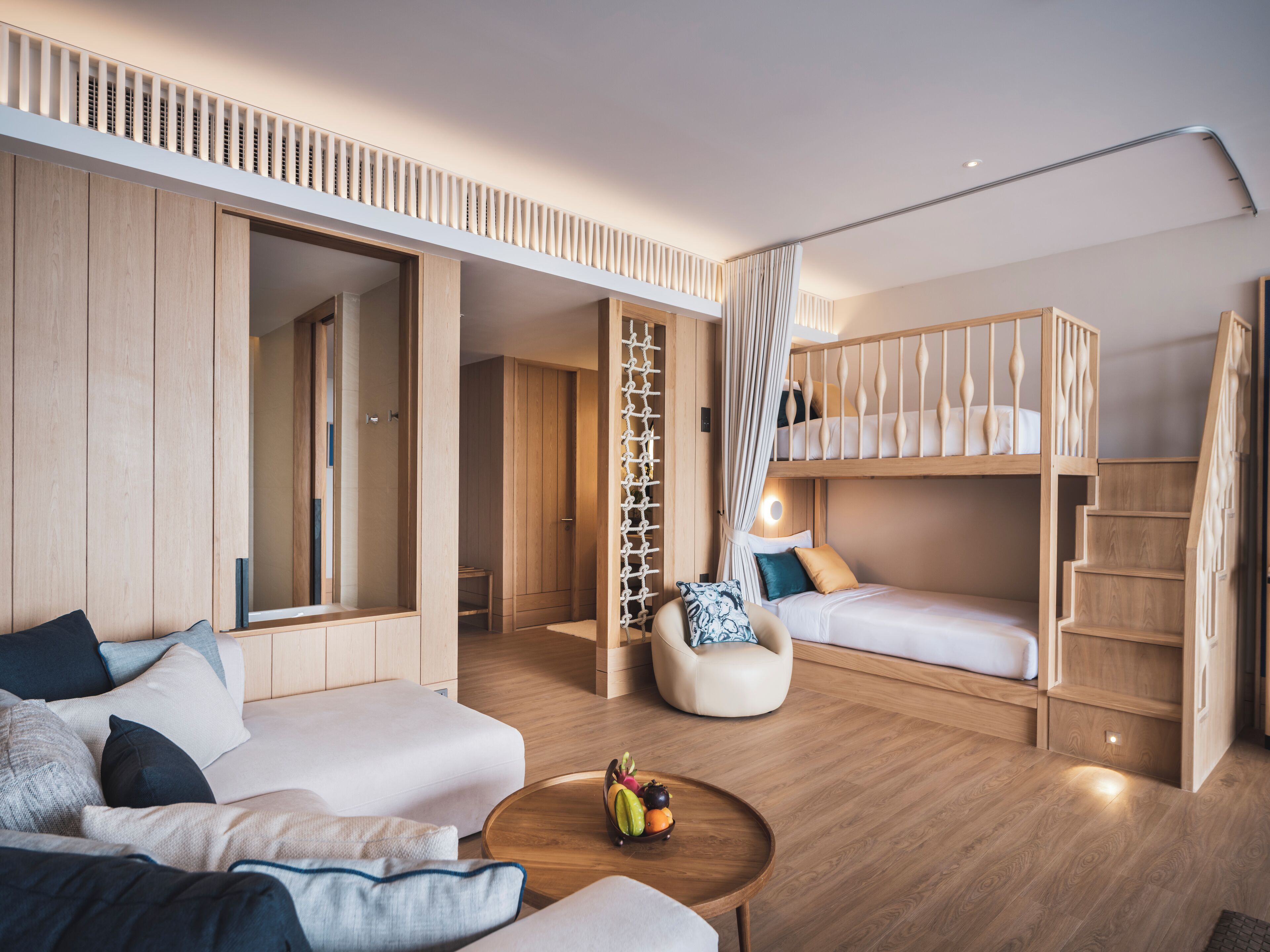 A modern, well-lit room with a bunk bed, a sofa, a coffee table with fruit, and wooden flooring.