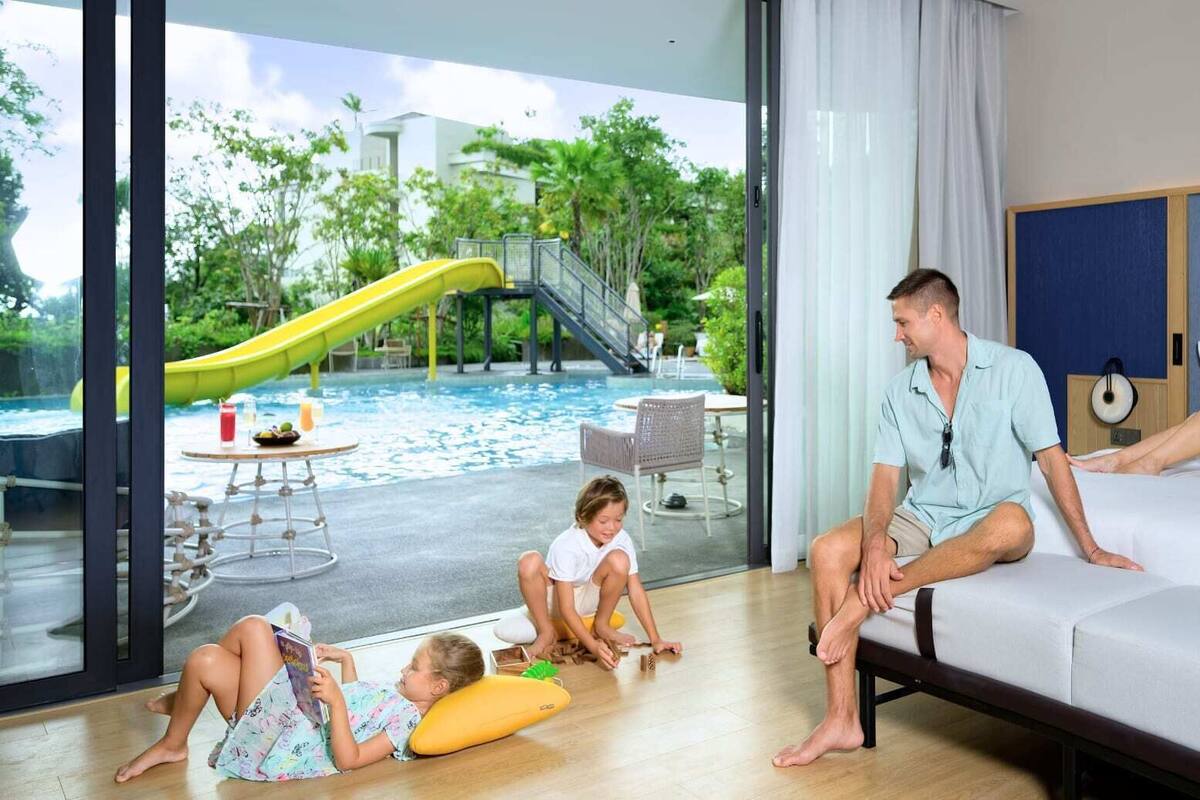 A hotel room with a bed, a sofa, and a view of a pool with a slide.