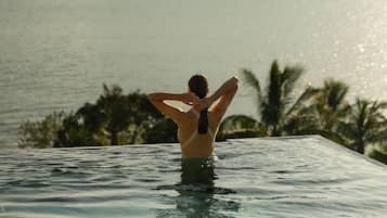 Eine Person im Schwimmbecken mit Blick auf eine große Insel und das Meer.