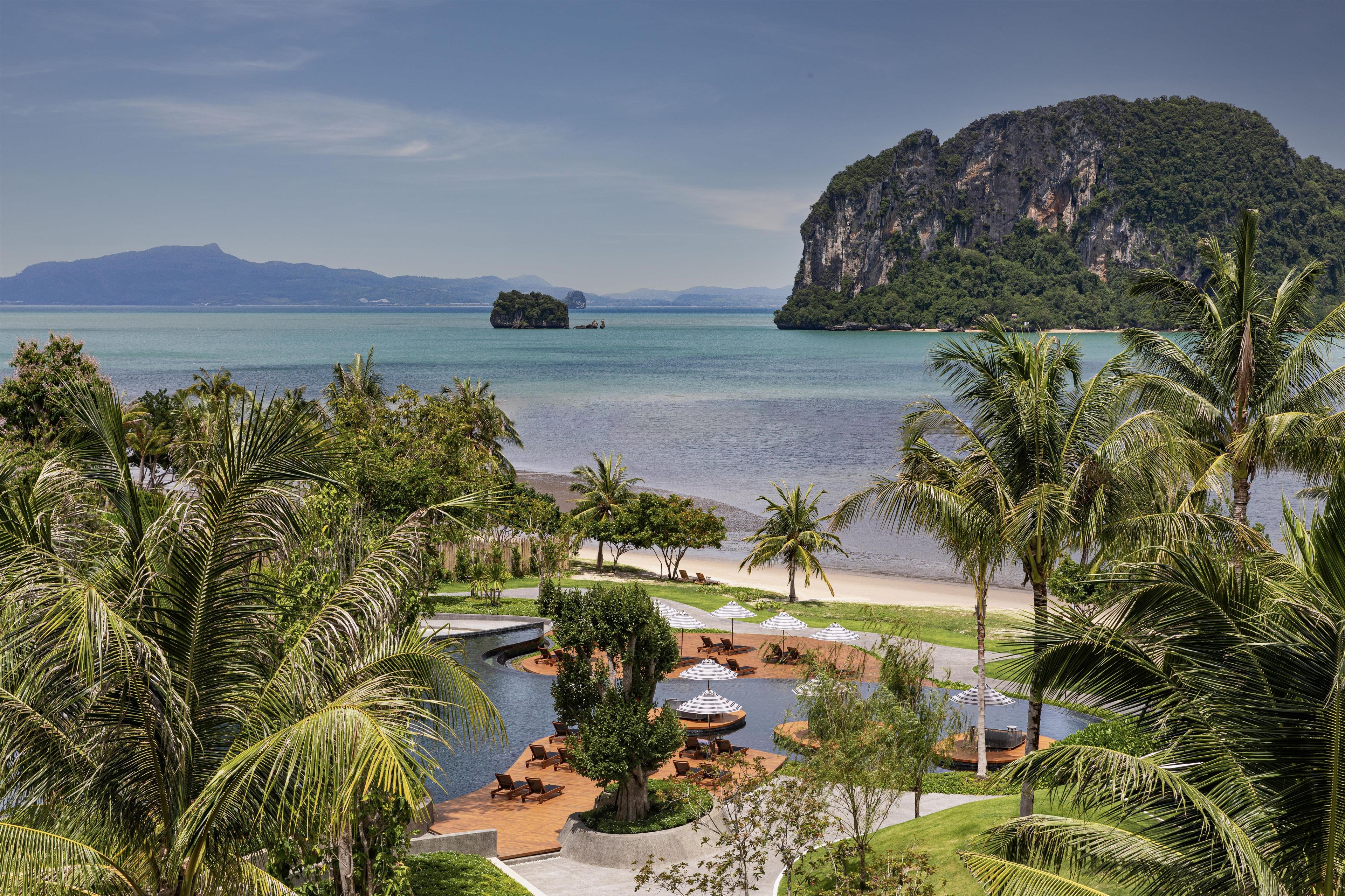 A resort with a pool area, lounge chairs, and a view of the sea and a large island.