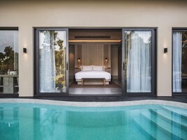 Un dormitorio moderno con una cama grande, puertas correderas de vidrio y vista a una piscina.
