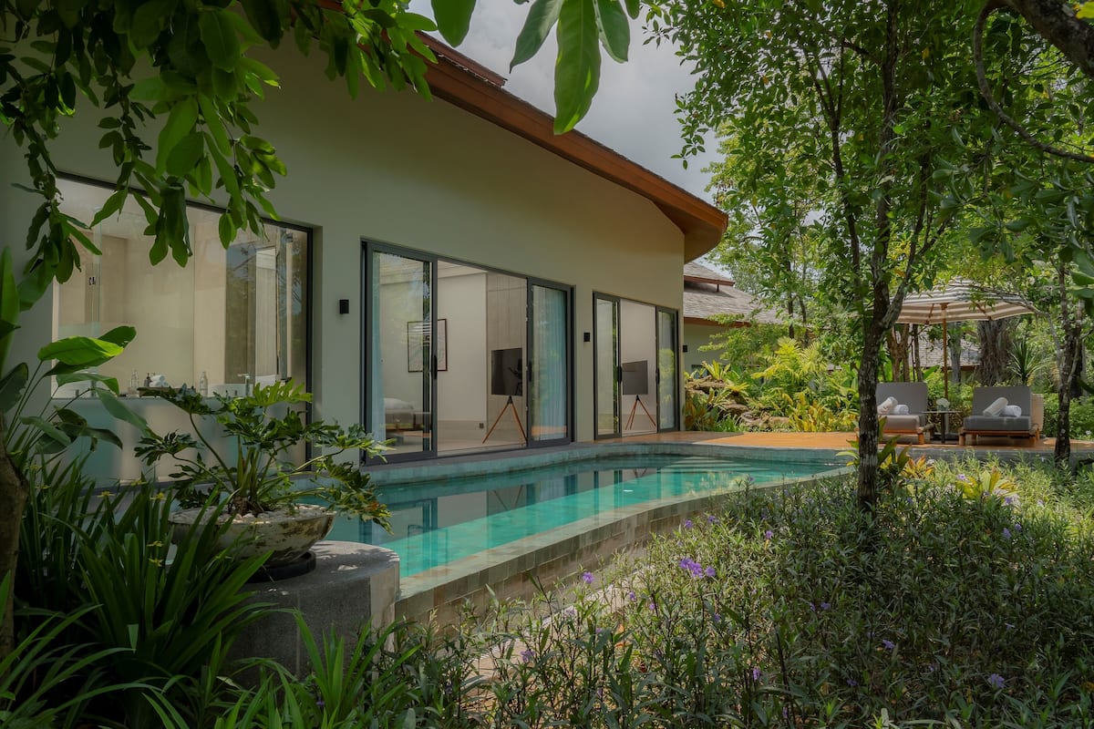 A modern house with a swimming pool, surrounded by lush greenery and a patio with lounge chairs.
