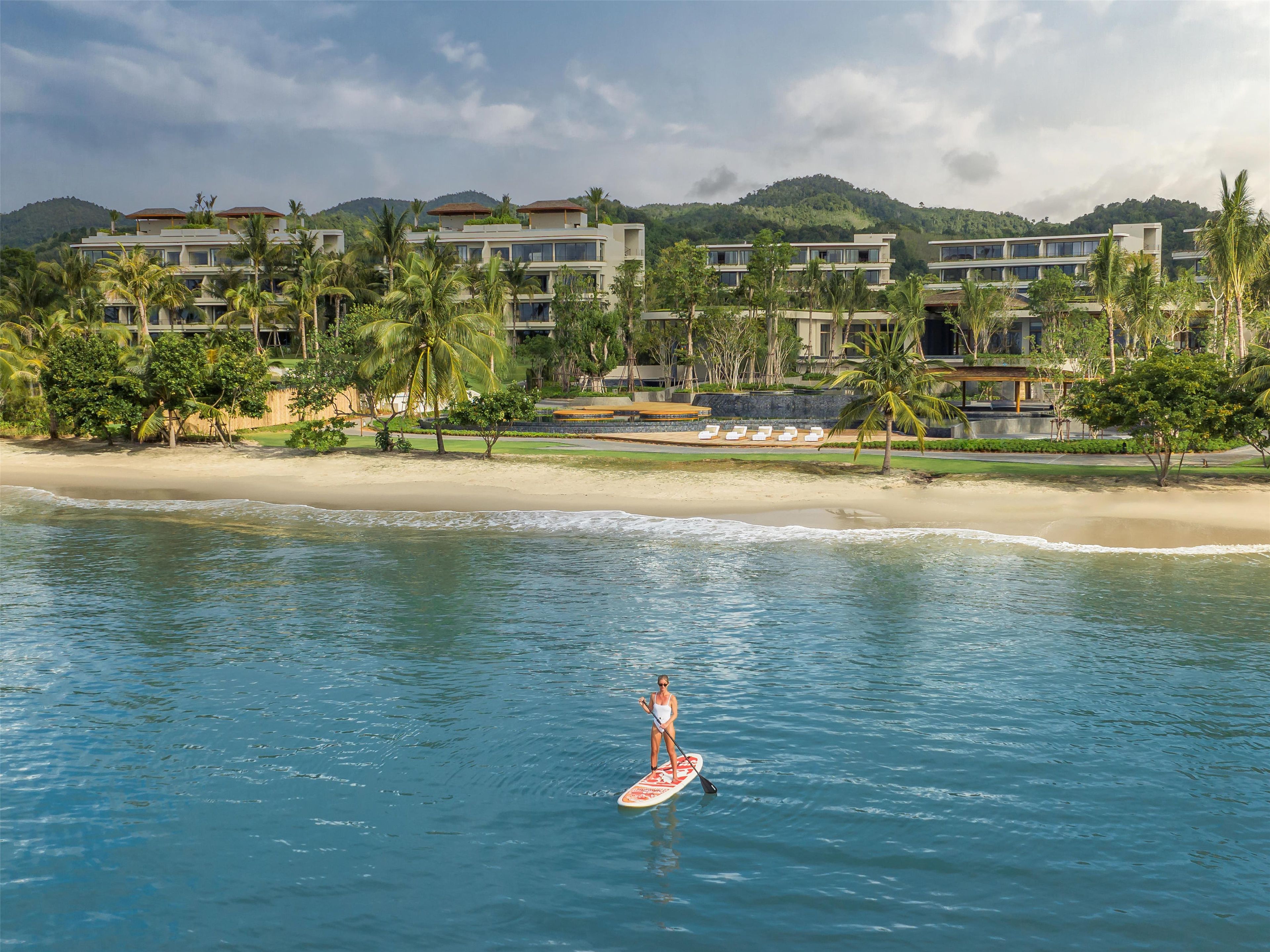 A resort with beachfront villas, a sandy beach, and a person paddleboarding.