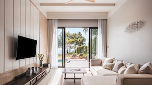 A modern living room with a flat-screen TV, a sofa, a coffee table, and a view of a pool and outdoor seating area. - Anantara Koh Yao Yai Resort & Villas (Ko Yao)