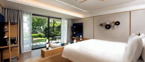 Una habitación de hotel moderna con una cama grande, muebles de madera, un televisor y un balcón con vistas a zonas verdes.