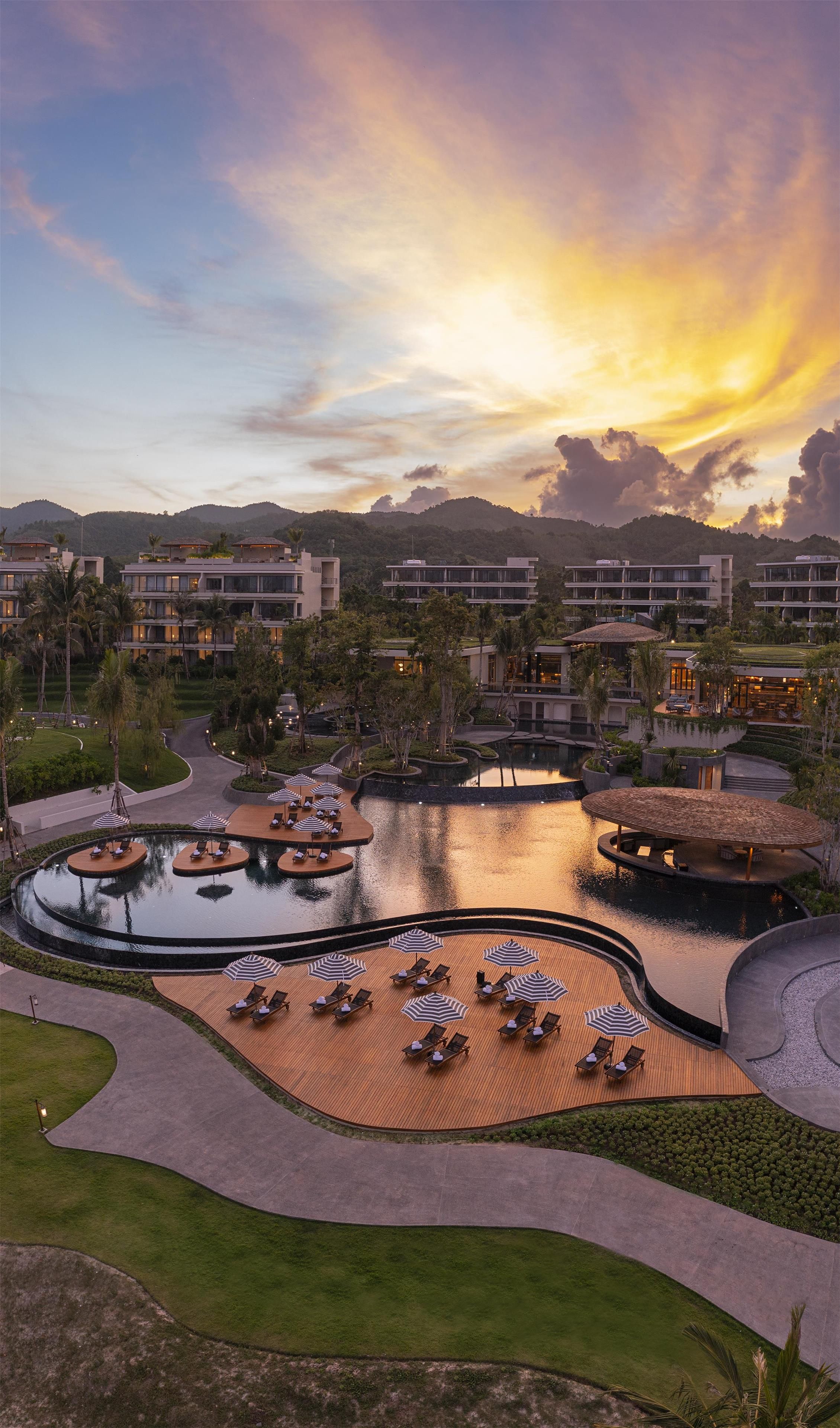 Ein Resort mit Poolbereich, Liegestühlen und Blick auf den Sonnenuntergang.