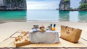 A beach picnic setup with food, drinks, and a woven bag on a mat. - Anantara Koh Yao Yai Resort & Villas (Ko Yao)