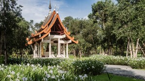 A traditional pavilion with a tiled roof, surrounded by lush greenery and white flowers.