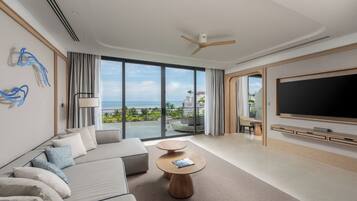 A modern hotel room with a large balcony, a sofa, a coffee table, and a flat-screen TV.