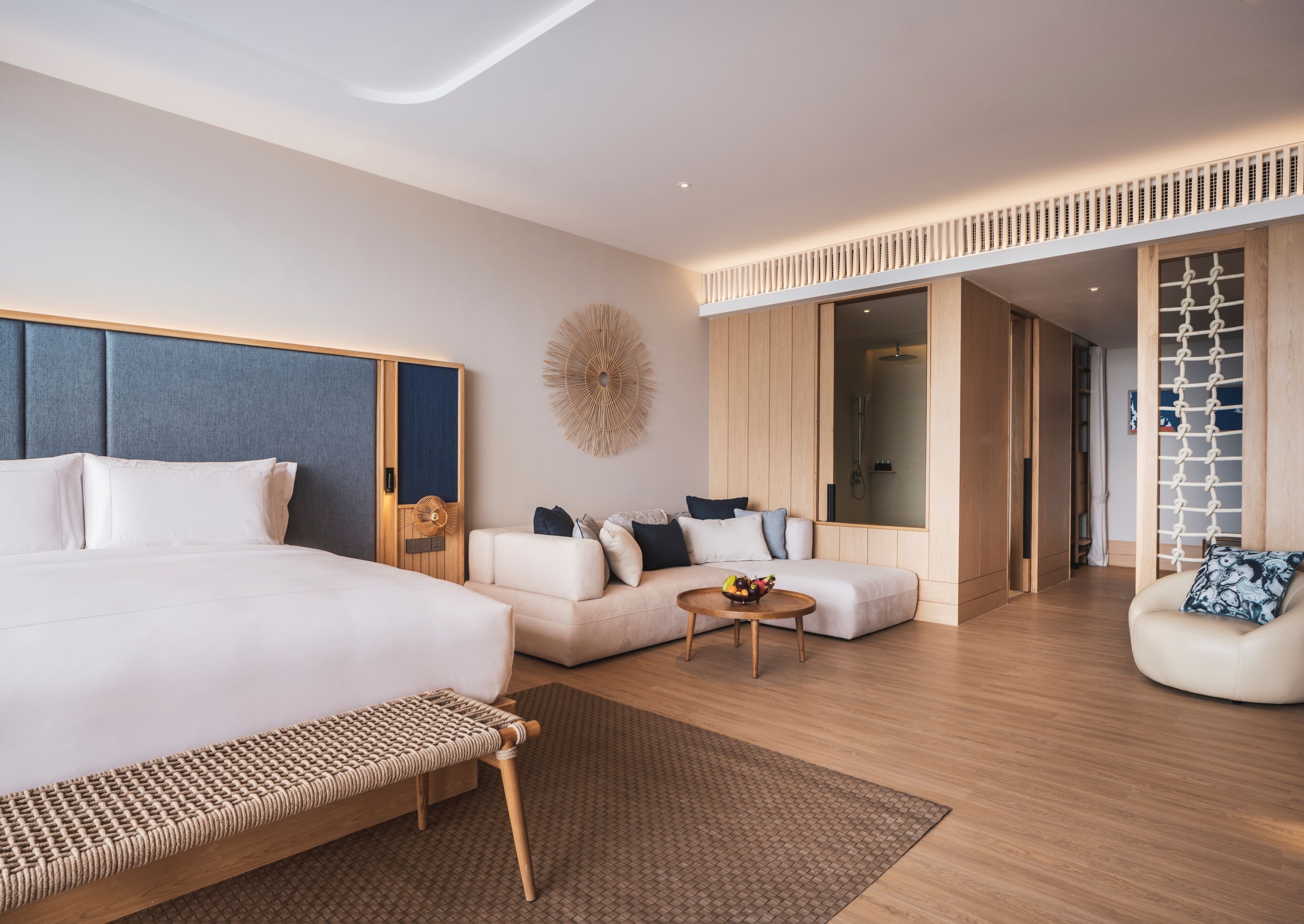 Ein modernes Hotelzimmer mit einem großen Bett, einer Couch, einem kleinen Tisch mit Früchten und einer begehbaren Dusche.