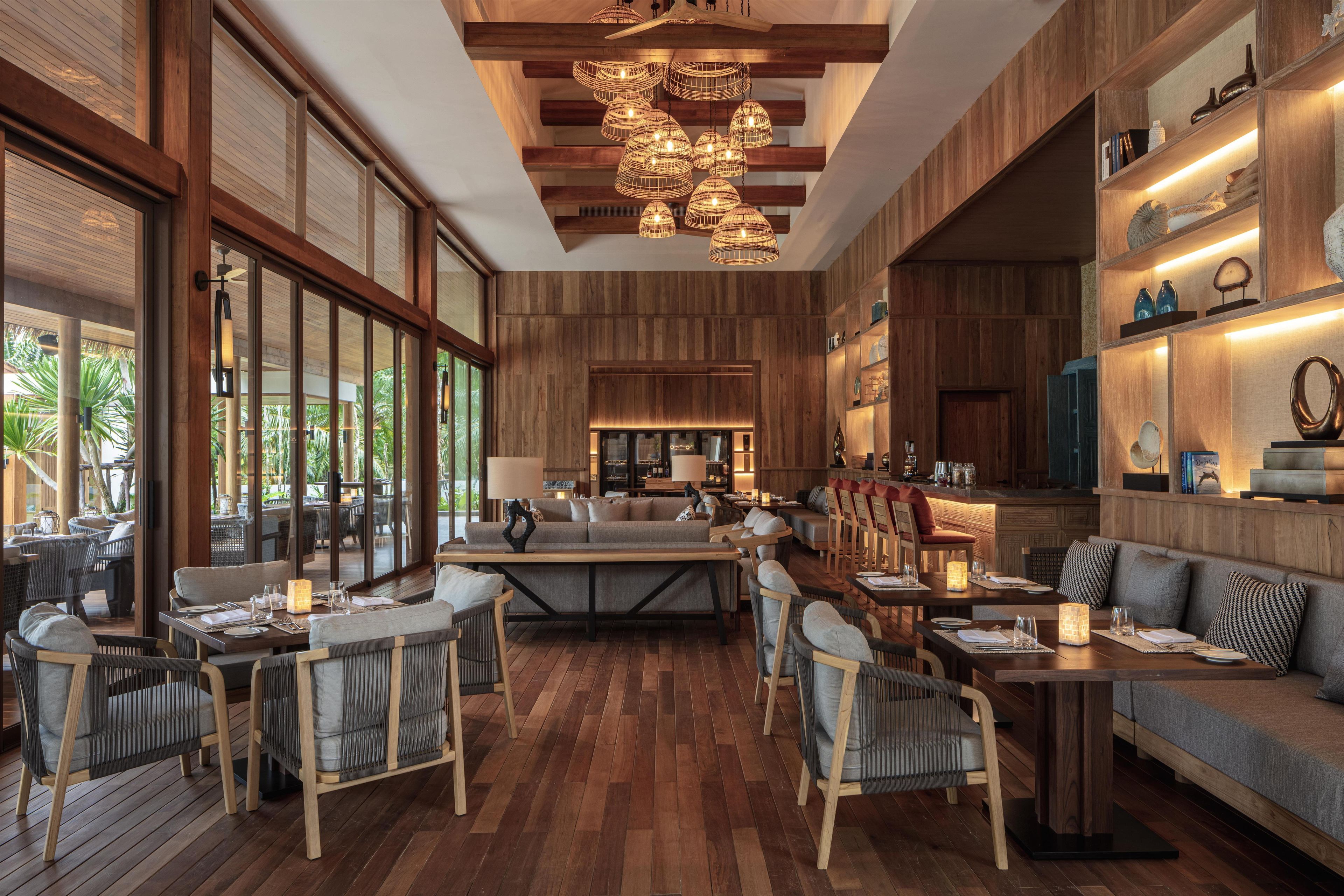 A spacious indoor area with wooden flooring, a central seating area with sofas and chairs, and a bar area with a counter.
