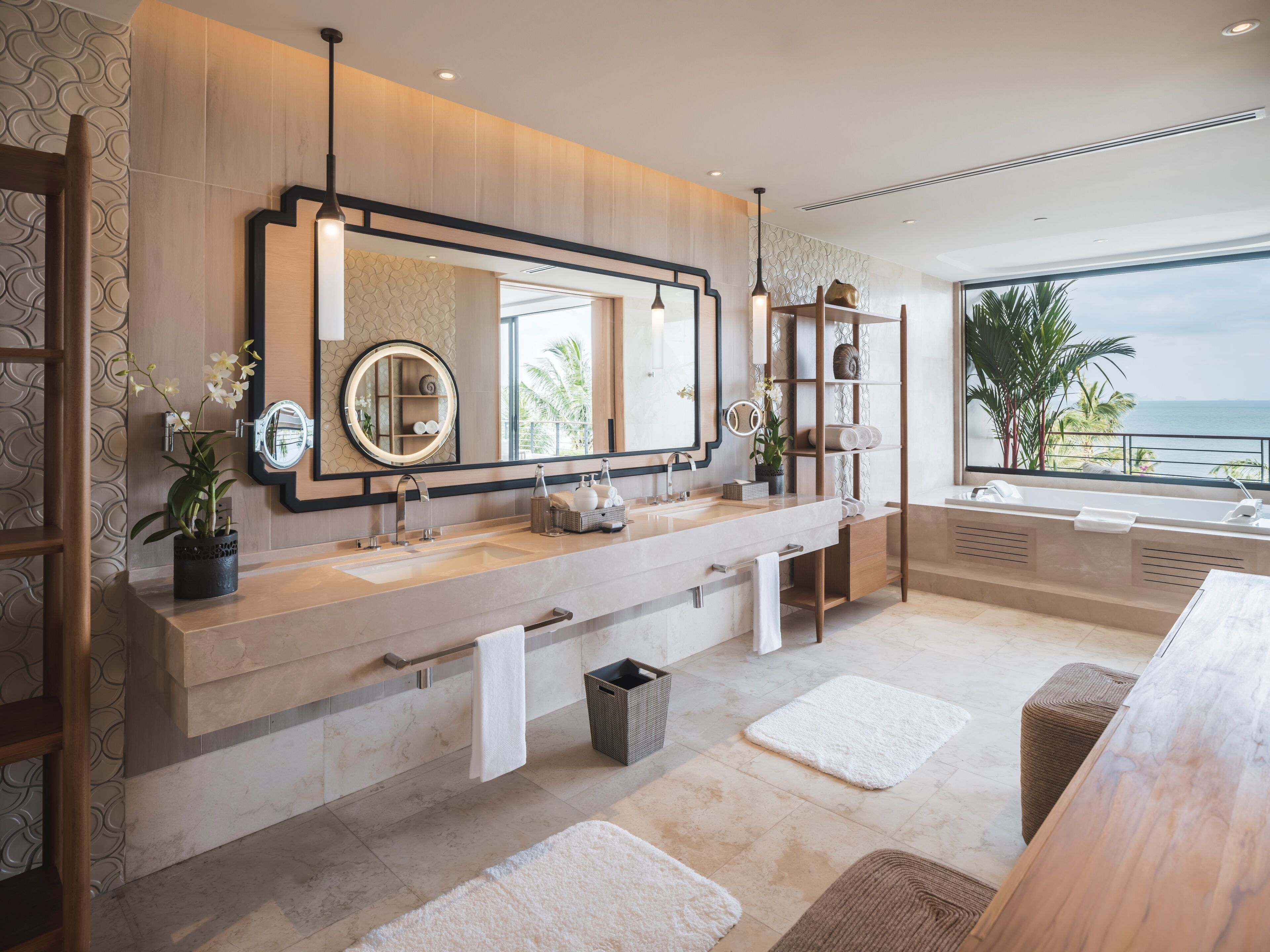 A modern bathroom with a large vanity, two sinks, a large mirror, and a view of the ocean.