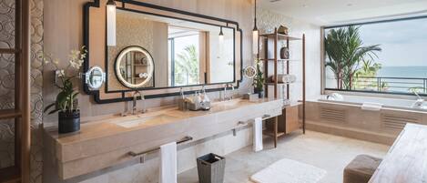 A modern bathroom with a large vanity, two sinks, a large mirror, and a view of the ocean.