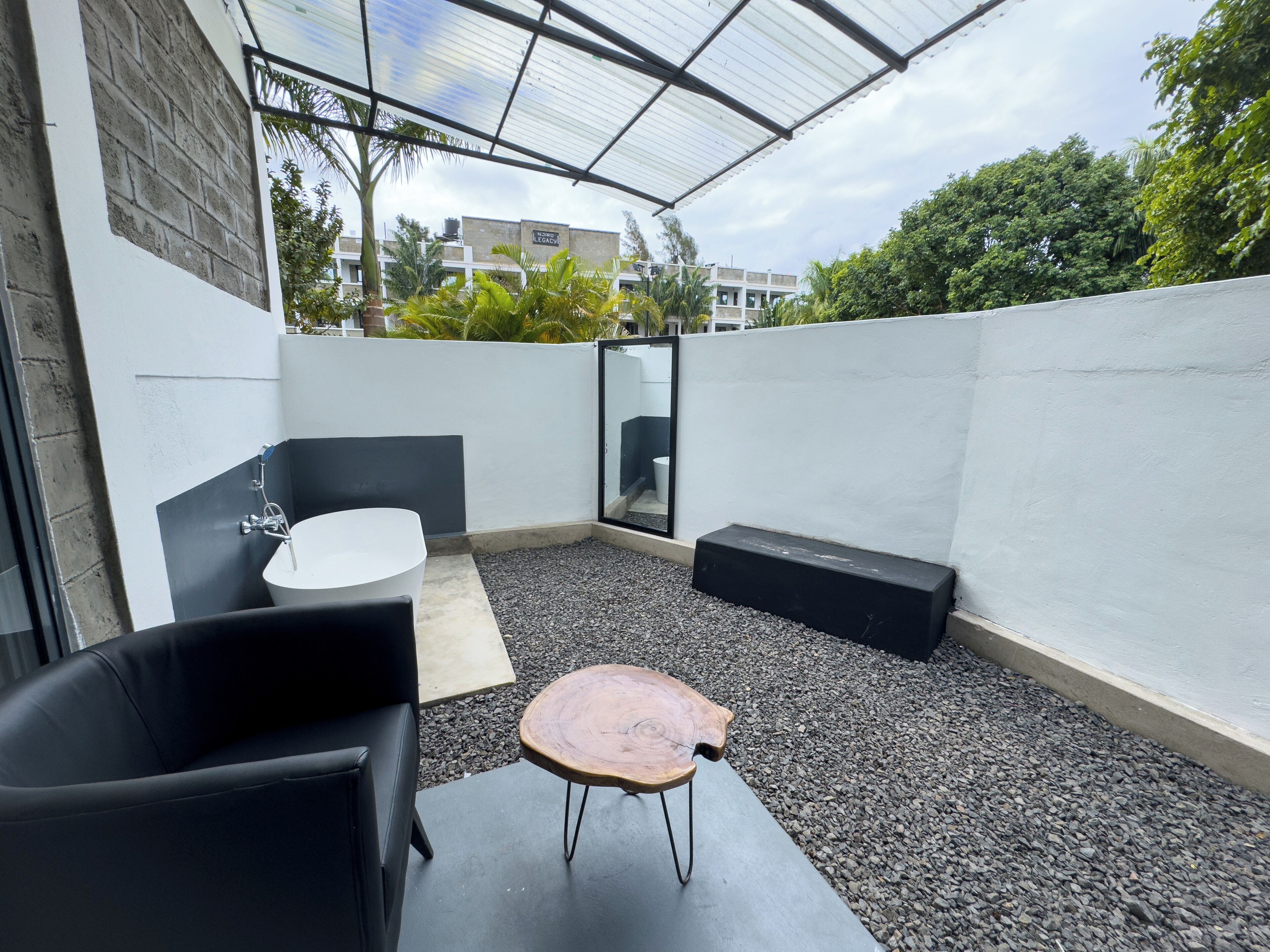 Un patio moderno al aire libre con un sofá de cuero negro, una mesa redonda de madera y un lavamanos blanco.