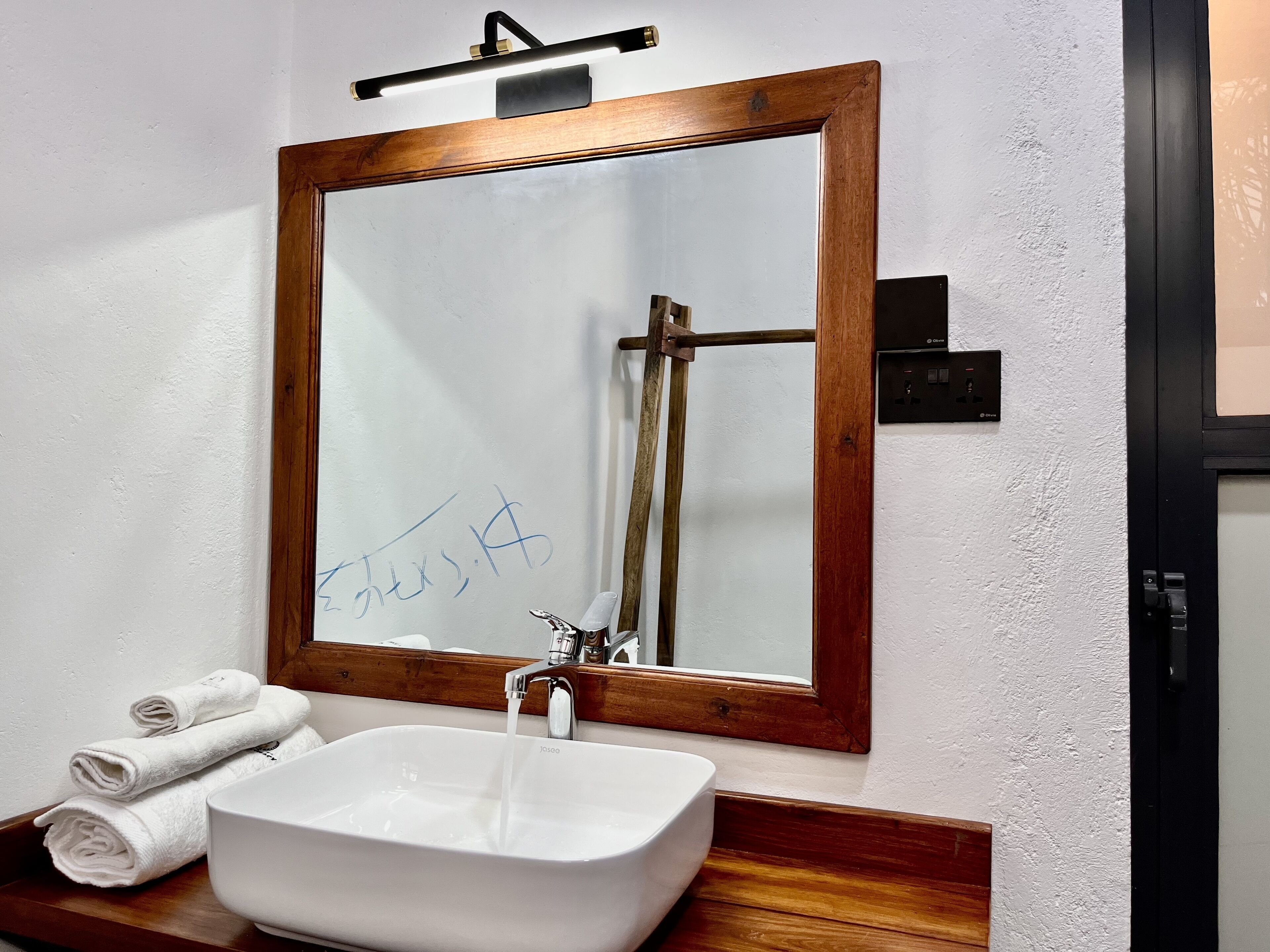 Een badkamer met een spiegel met houten lijst, een witte wastafel en een handdoekrek met handdoeken.