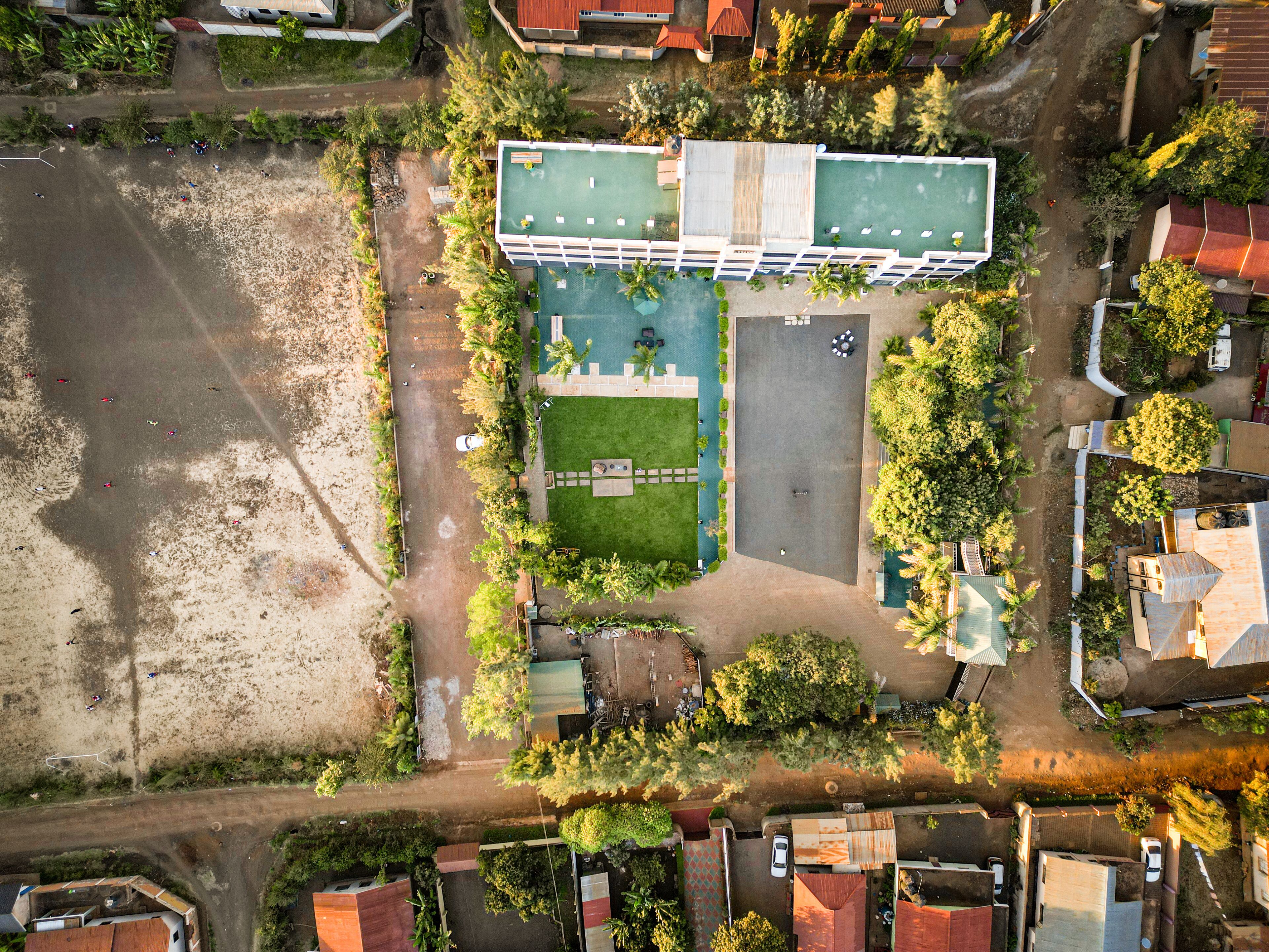An aerial view of a building with a green roof, a swimming pool, and a parking area.