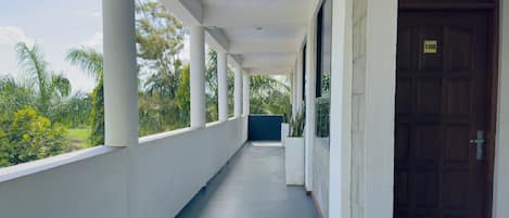 A covered corridor with white columns, a dark floor, and a wooden door with a number plate.