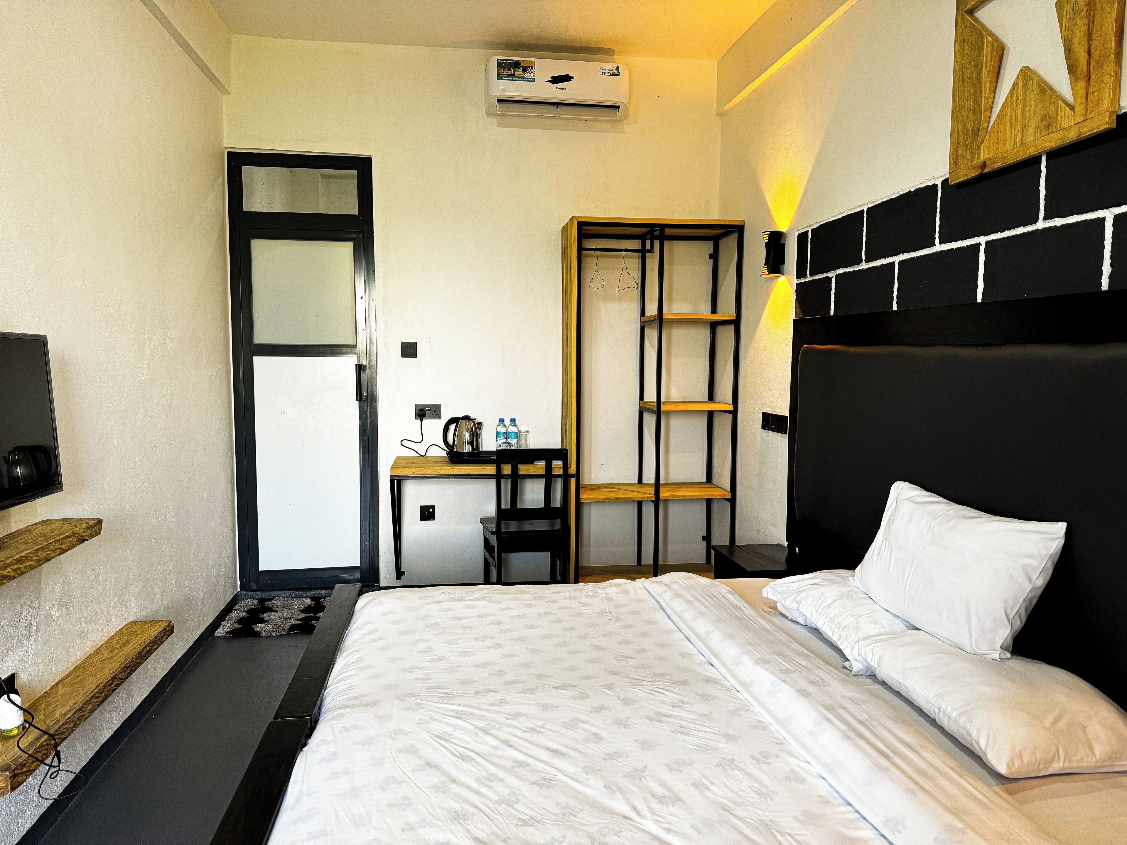 A hotel room with a bed, a desk with a chair, a TV, and a wardrobe.