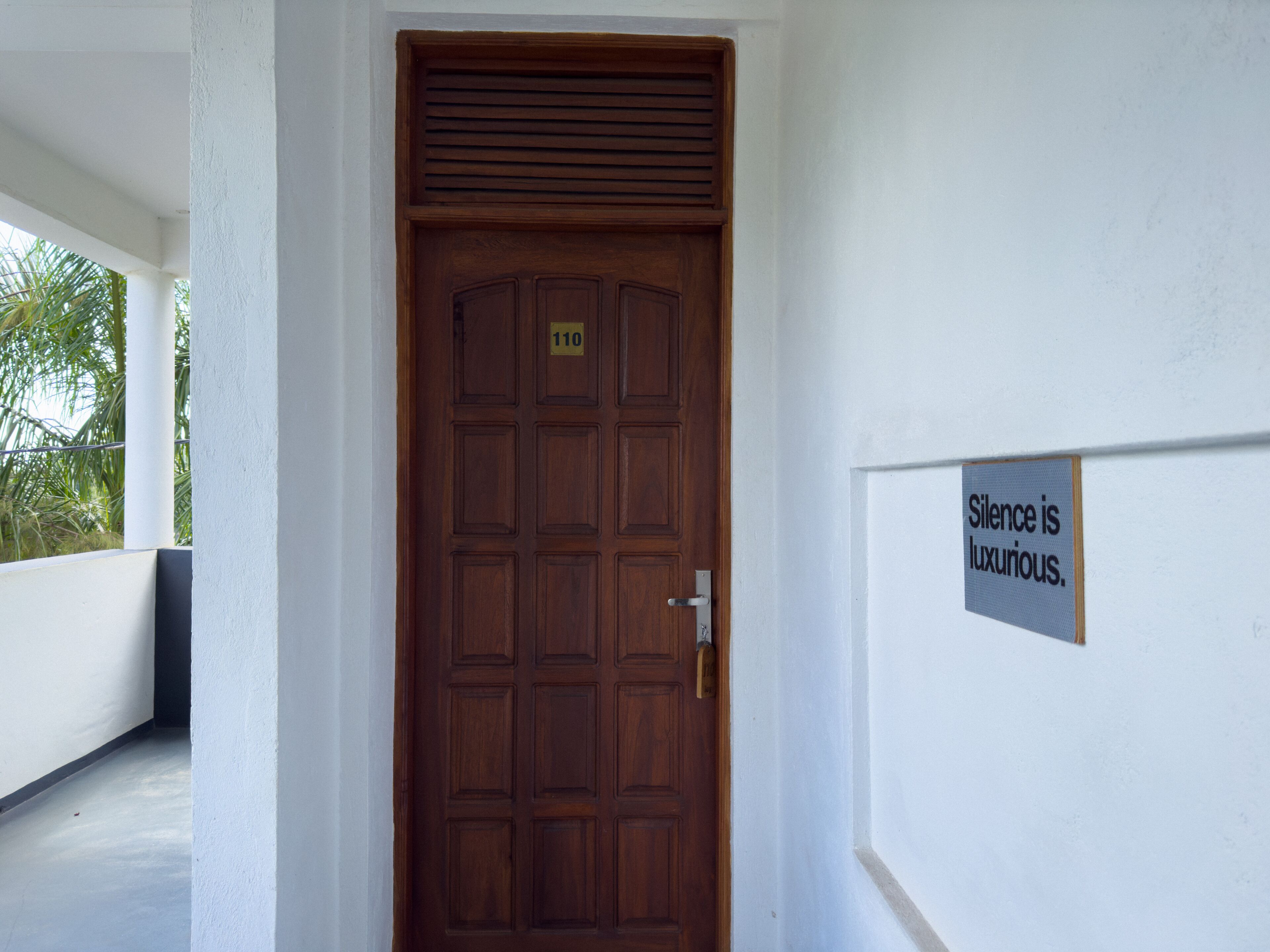 Uma porta de madeira com uma placa de número e um aviso que diz: "Silêncio é luxo".