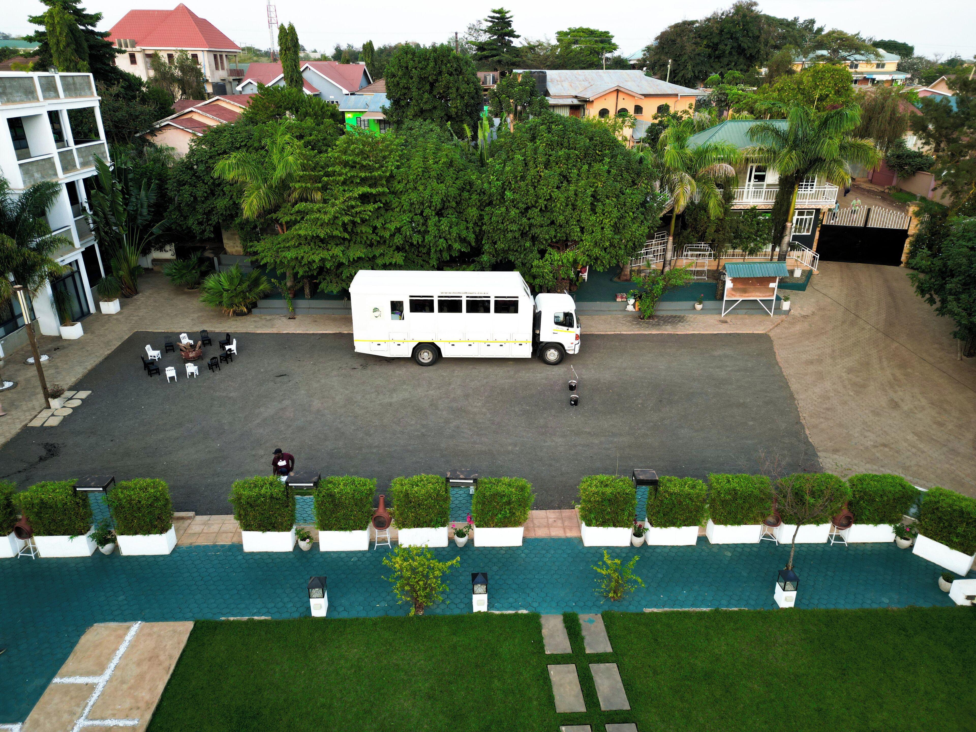 A parking area with a white bus, outdoor seating, and well-maintained greenery.