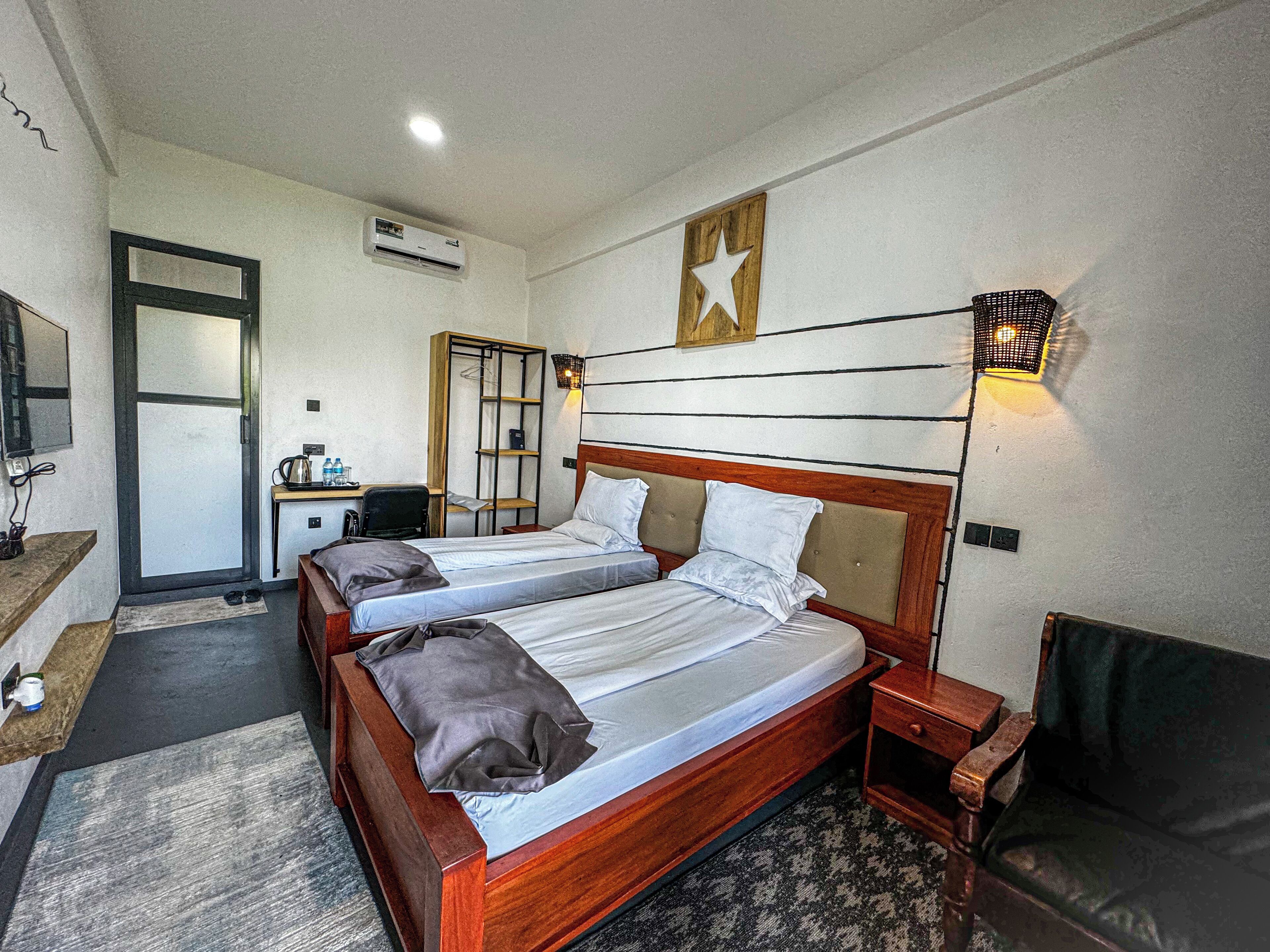 A hotel room with two beds, a desk, a chair, a small table, a sofa, a wall-mounted TV, a star decoration, and a wall-mounted light fixture.