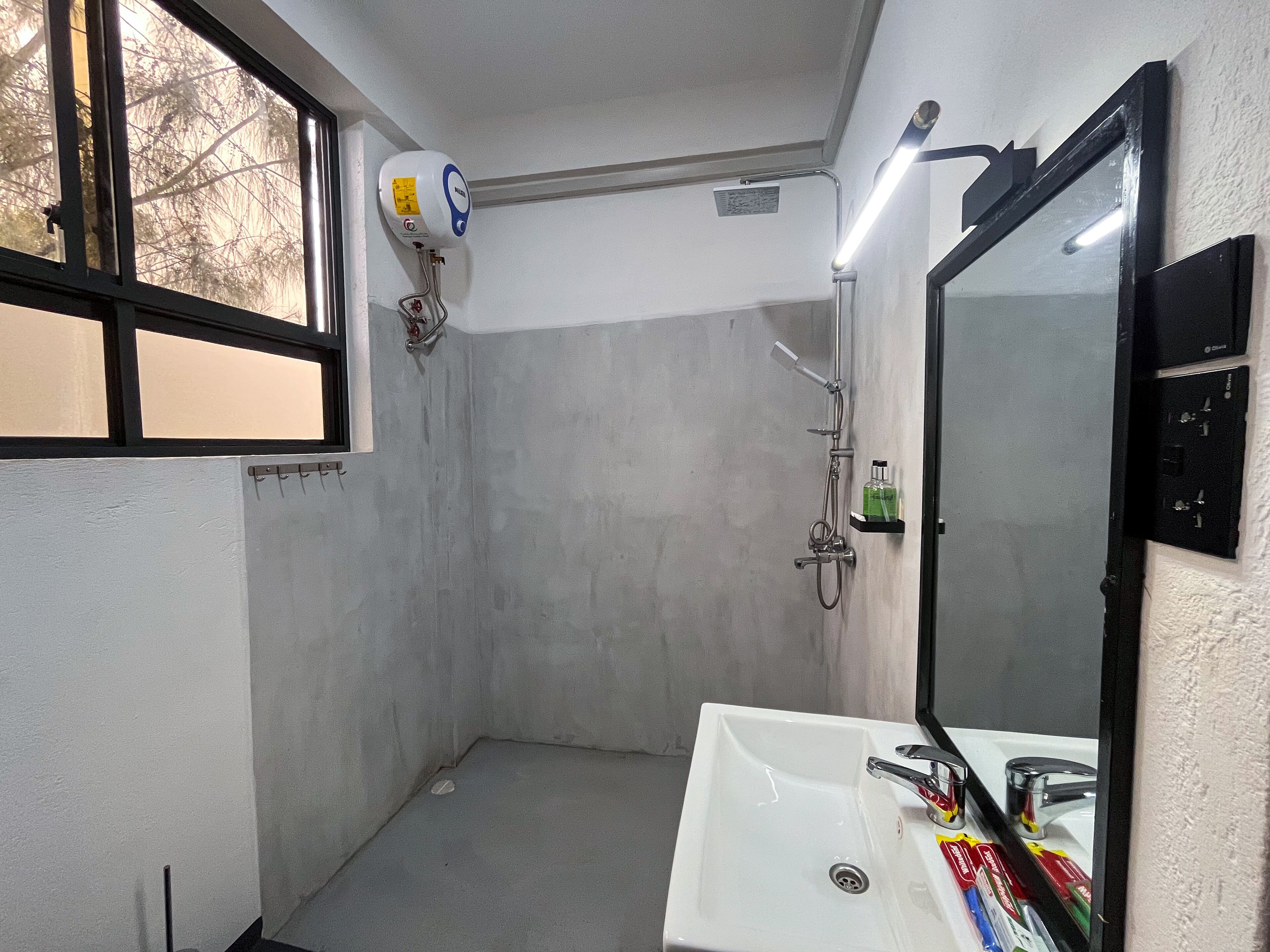 Un baño pequeño con ventana, ducha, lavamanos y espejo.