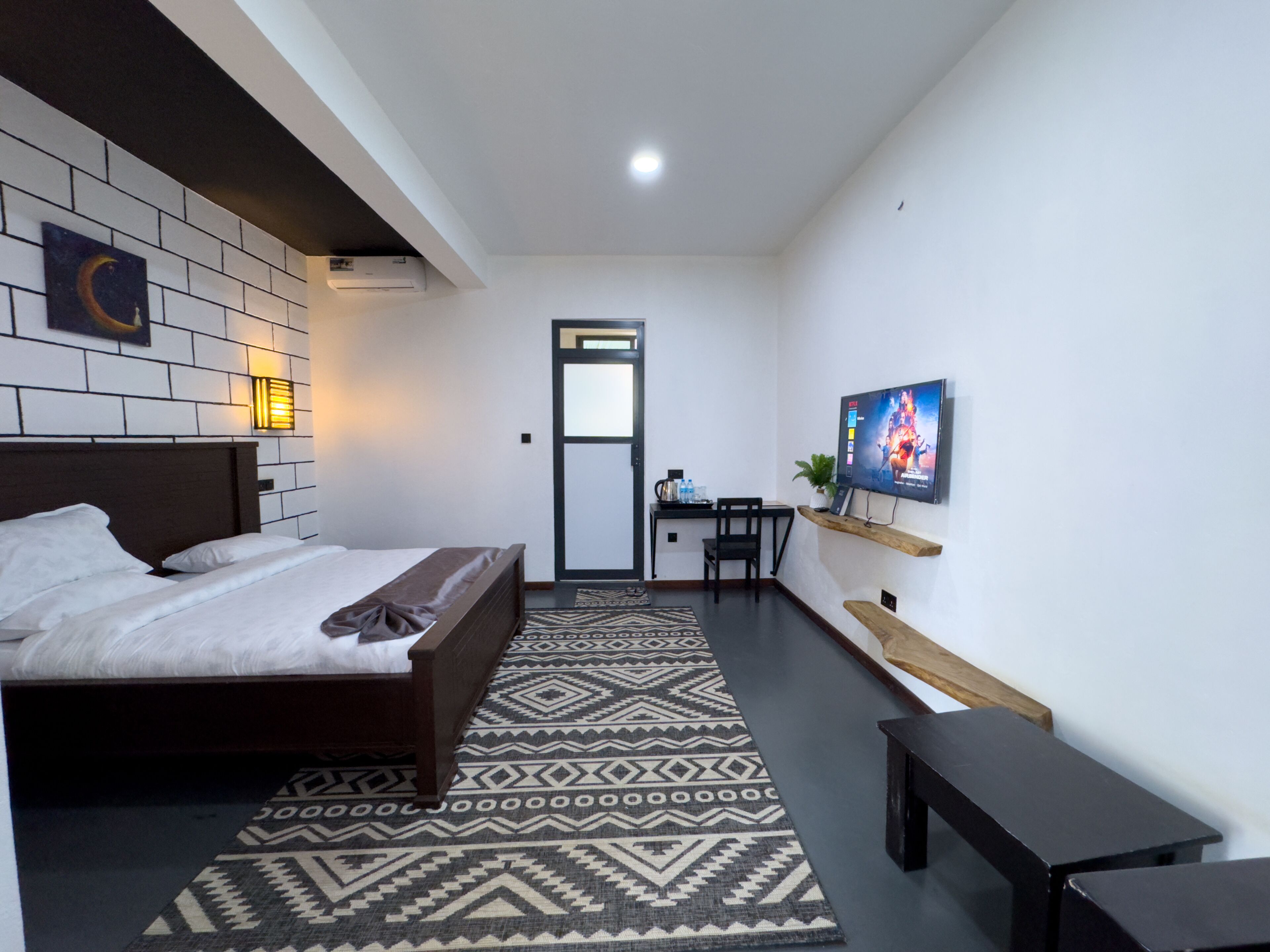 A modern hotel room with a bed, a desk, a chair, a television, and a patterned rug.