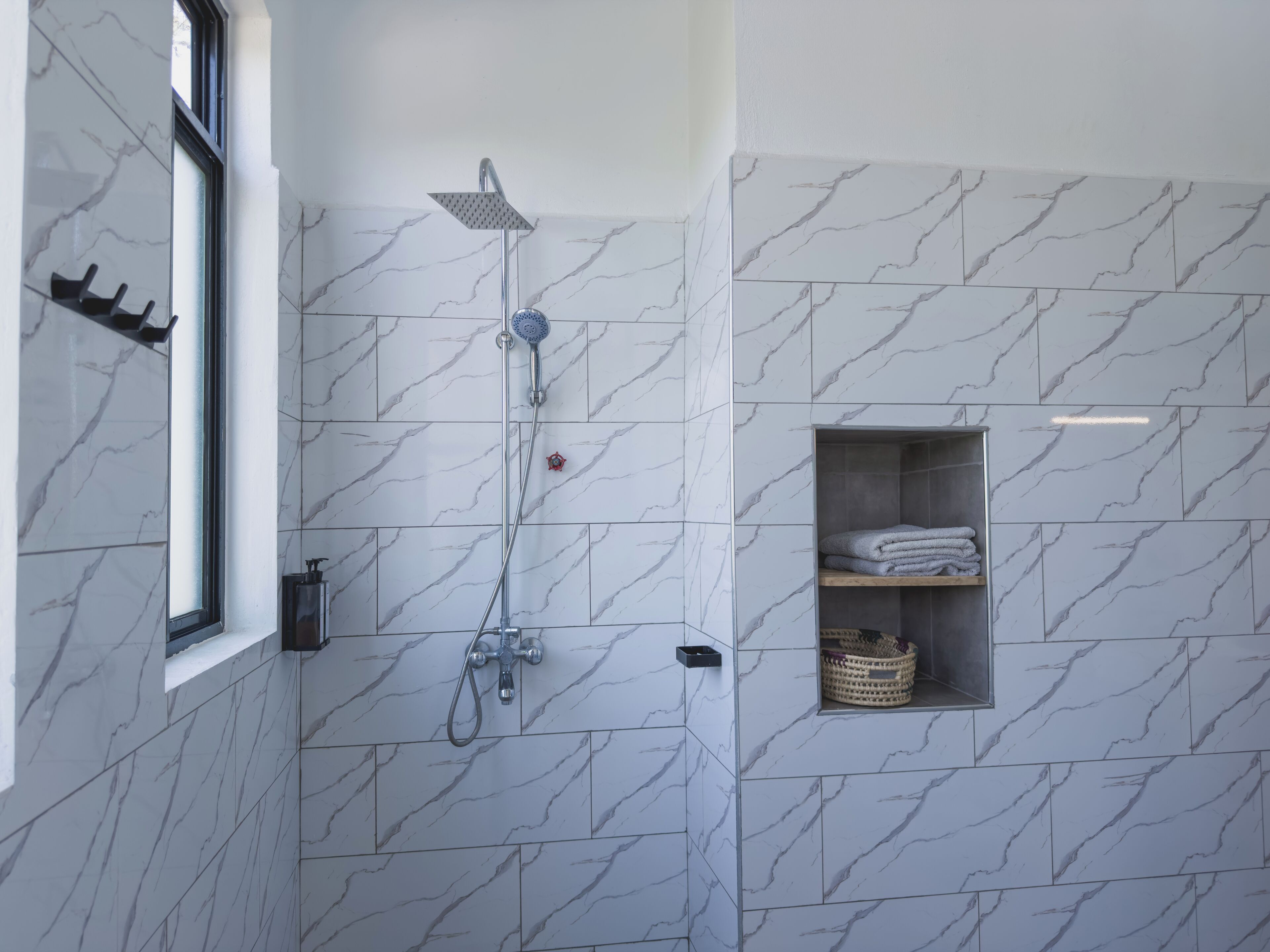 Une salle de bain moderne avec une douche, des carreaux de marbre, une fenêtre et une étagère avec des serviettes.