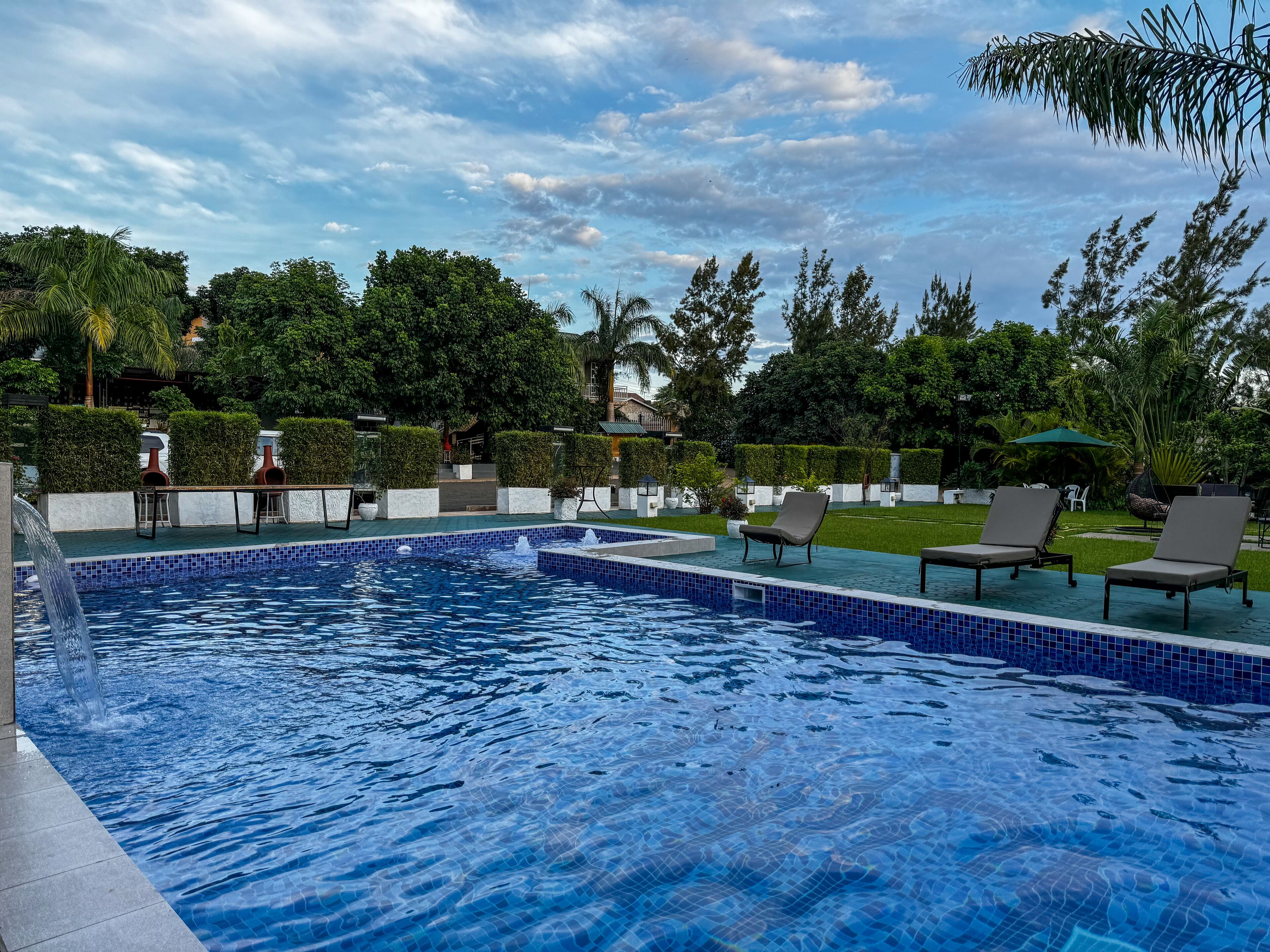 A swimming pool with tiled edges, surrounded by lounge chairs and a well-maintained garden.