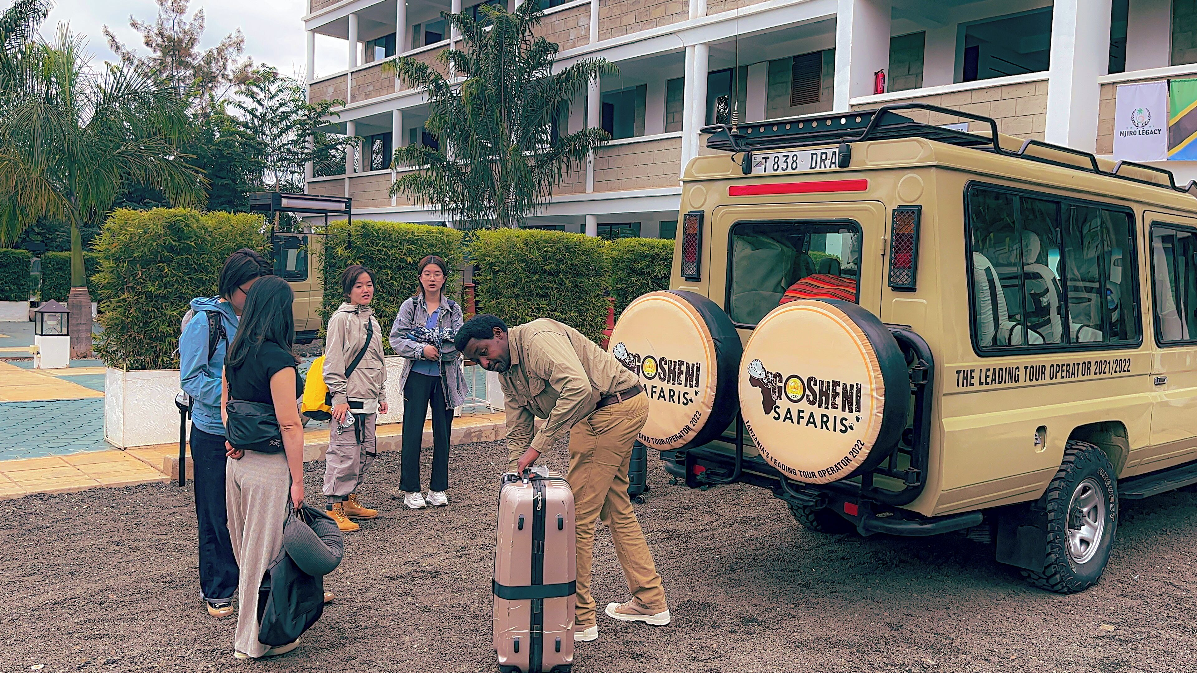 Un vehículo safari con la marca "GOSHENI SAFARIS" estacionado frente a un edificio con varios balcones.