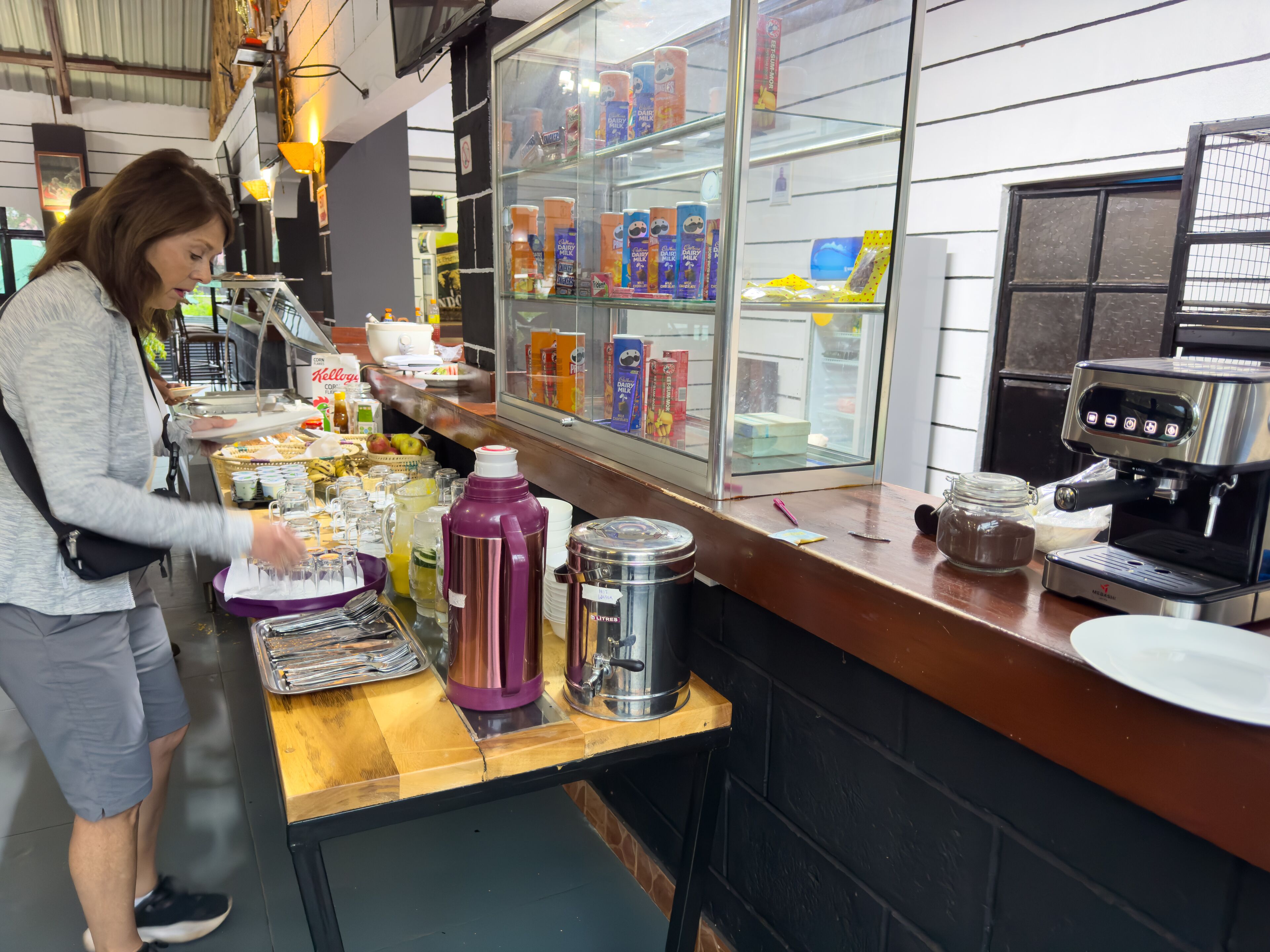 A café counter with a coffee machine, a refrigerator stocked with beverages, and a variety of food items.