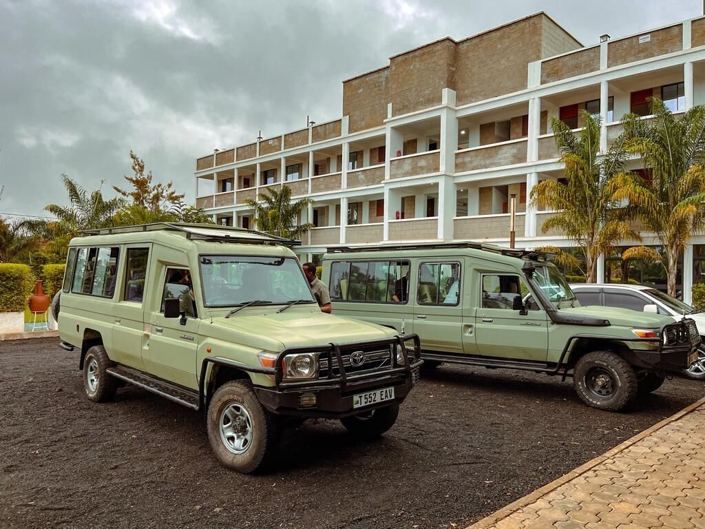 Deux véhicules tout-terrain sont stationnés devant un immeuble à plusieurs étages, doté de balcons.