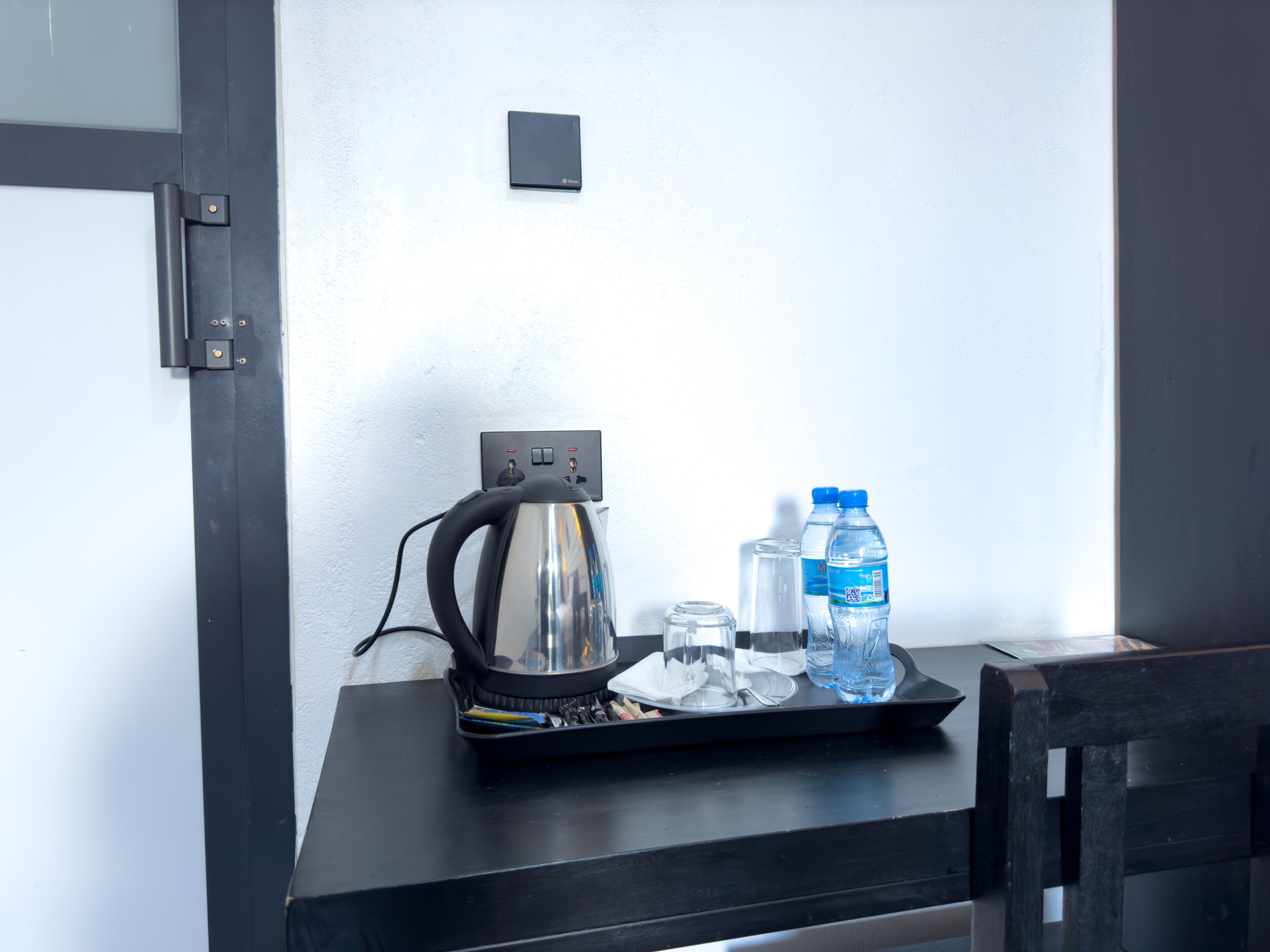 A table with a kettle, two water bottles, and a tray with glasses and utensils.