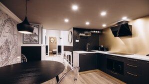 A modern kitchen with dark cabinetry, a white countertop, and a dining area with a round table and chairs. - Native Apartments Paulińska 20 (Kraków)
