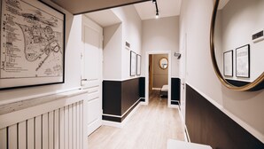 A hallway with a wooden floor, white walls, and a black and white patterned wall hanging. There is a door at the end of the hallway. - Native Apartments Paulińska 20 (Kraków)