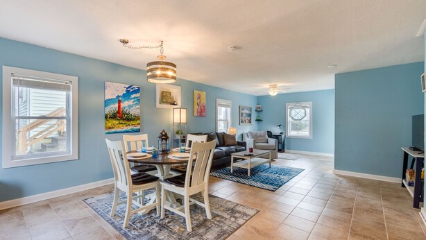 A spacious living room with a dining area, featuring a large window, a chandelier, and a blue wall. - Pet Friendly - 2 Minute Walk to Beach -  Updated and Modernized Spotless Clean  (Kill Devil Hills)