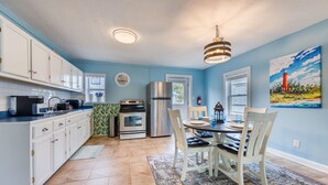 A kitchen with white cabinets, a stainless steel refrigerator, a microwave, and a stove. There is a dining table with chairs and a rug. - Pet Friendly - 2 Minute Walk to Beach -  Updated and Modernized Spotless Clean  (Kill Devil Hills)