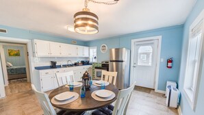 A compact kitchen with white cabinets, a stainless steel refrigerator, and a dining area with a round table and chairs. - Pet Friendly - 2 Minute Walk to Beach -  Updated and Modernized Spotless Clean  (Kill Devil Hills)