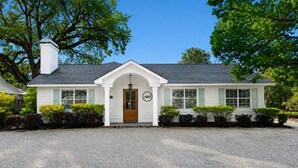 Une maison de plain-pied à l’extérieur blanc, avec un toit foncé et une porte d’entrée en bois.