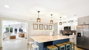 Une cuisine moderne dotée d’un îlot central, de meubles blancs, d’appareils électroménagers en acier inoxydable et d’un coin repas avec des tabourets de bar.