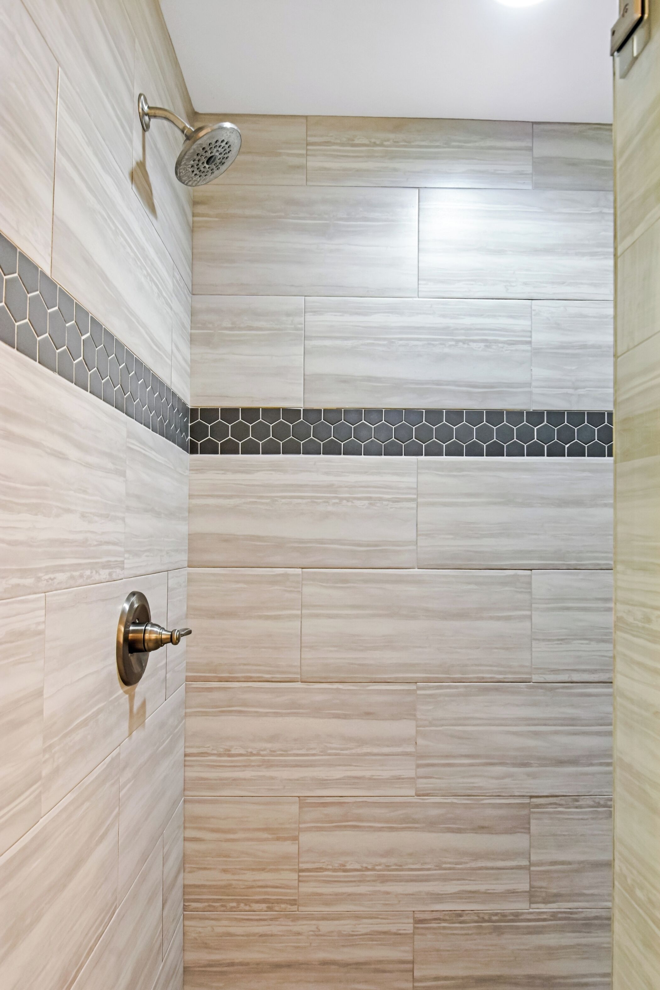 A shower with a handheld showerhead, a metallic door handle, and a tiled wall with a geometric pattern.
