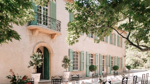 A two-story building with a balcony, a dining area set up with tables and chairs, and a large archway entrance. - Private castle with swimming pool in Provence (Lamanon)