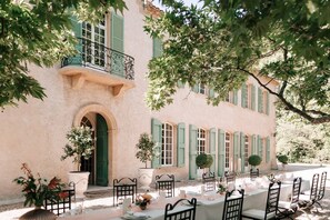 A two-story building with a balcony, a dining area set up with tables and chairs, and a large archway entrance.